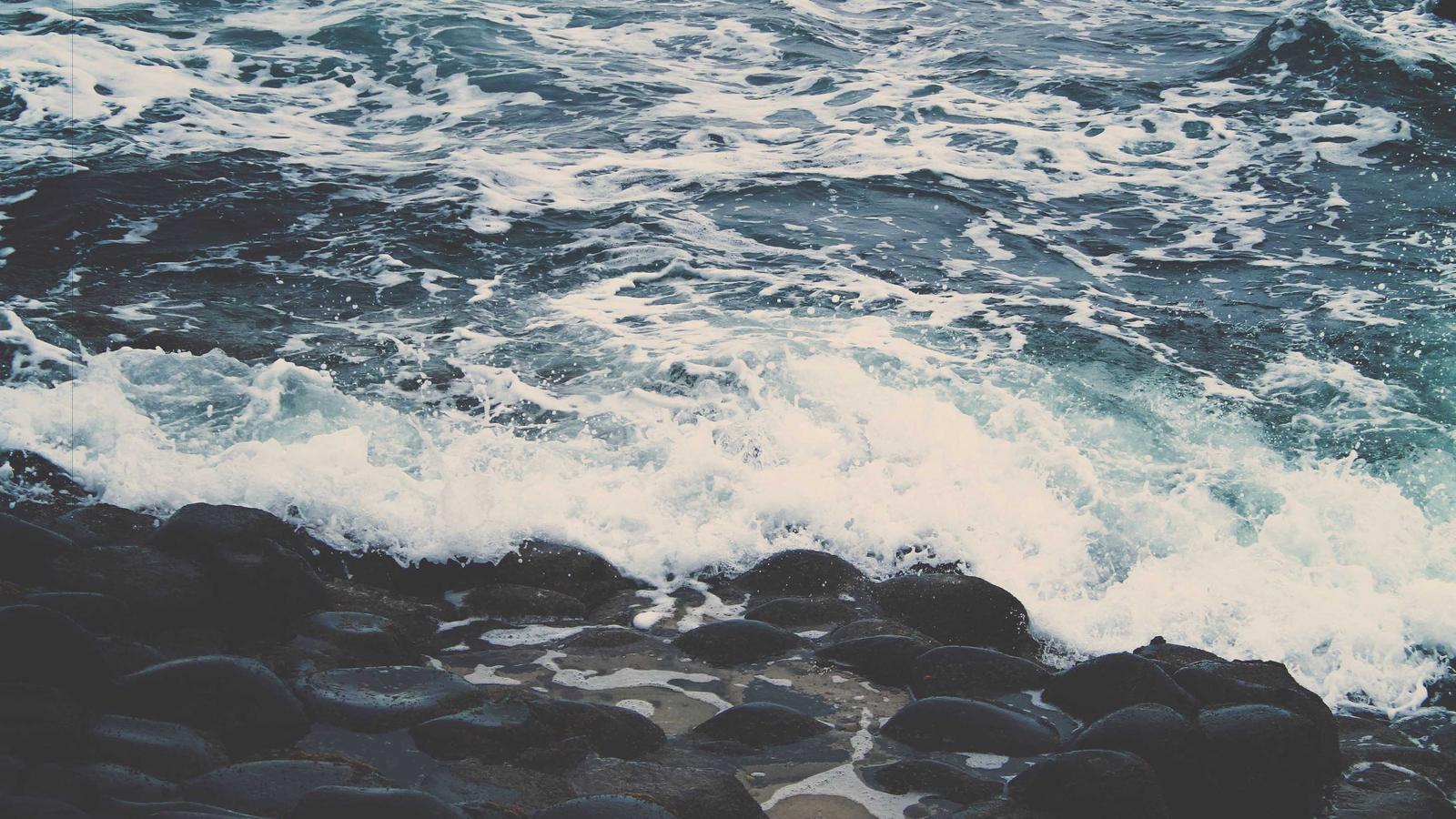 A vintage luxury train running on tracks through a forested mountain landscape in Japan during autumn with red and gold maple leaves visible on either side of the rail line and a small lake beyond.