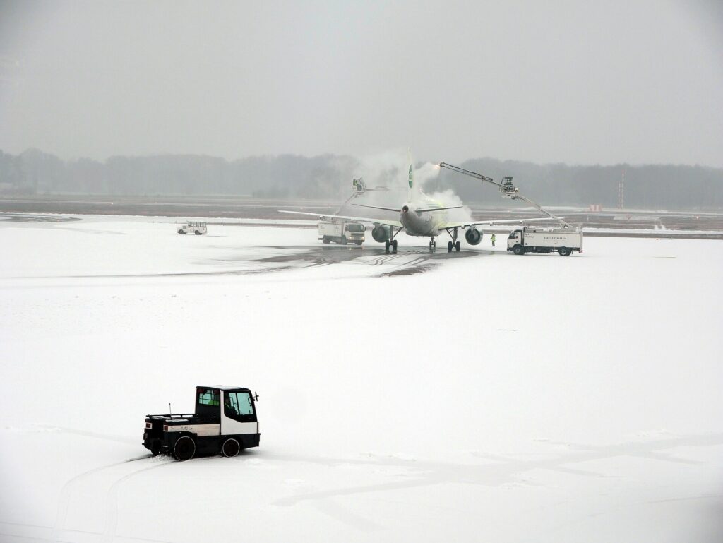 Camion de dégivrage aspergeant l'aile d'un avion sur une aire enneigée au petit matin