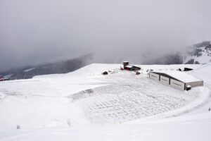Piste enneigée descendant vers les toits d'une station avec des skieurs à l'approche