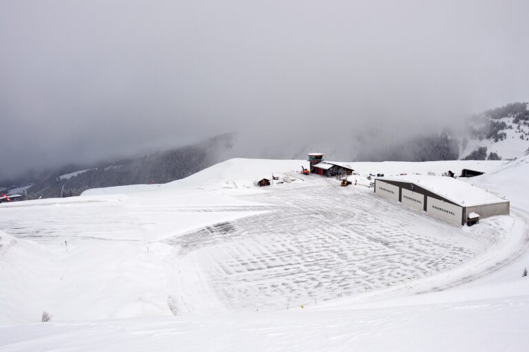 Piste enneigée descendant vers les toits d'une station avec des skieurs à l'approche