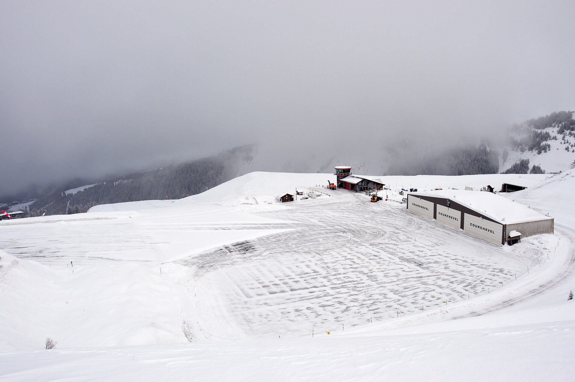 Piste enneigée descendant vers les toits d'une station avec des skieurs à l'approche