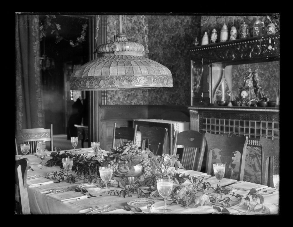 Verres à vin alignés sur une nappe blanche, carafe et bouteille posées à côté d'un couvert