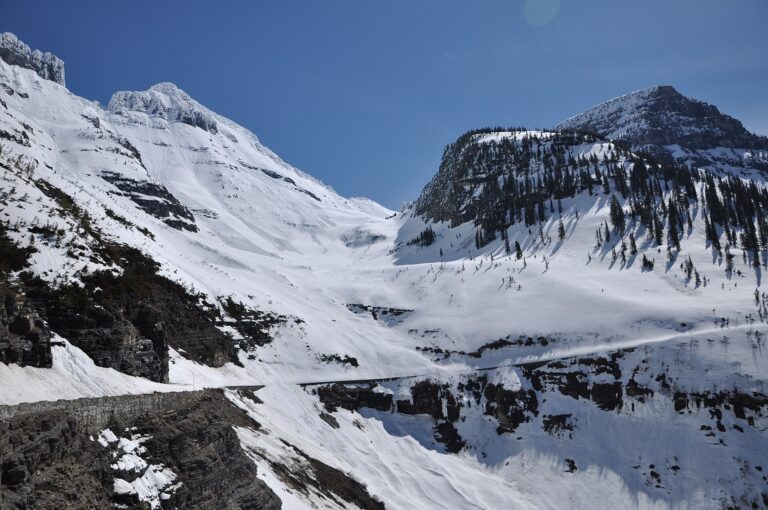 Piste damée sur un glacier d'altitude, neige dure et crêtes rocheuses dégagées à l'arrière-plan