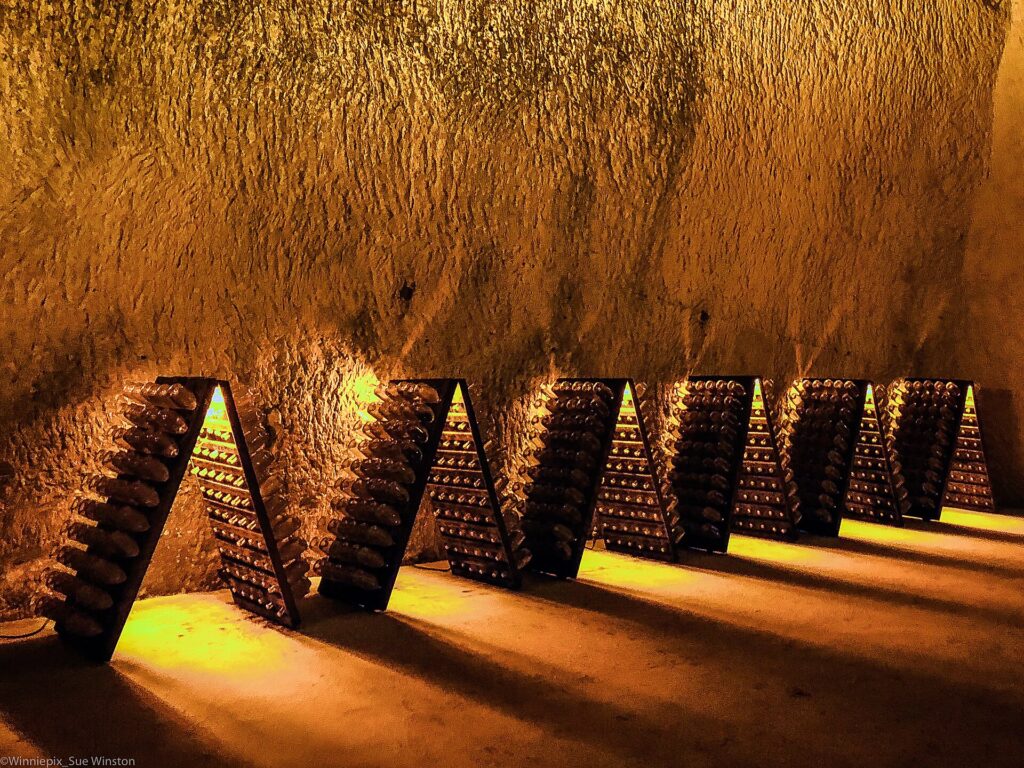 Pupitres de remuage en bois garnis de bouteilles inclinées dans une cave voûtée
