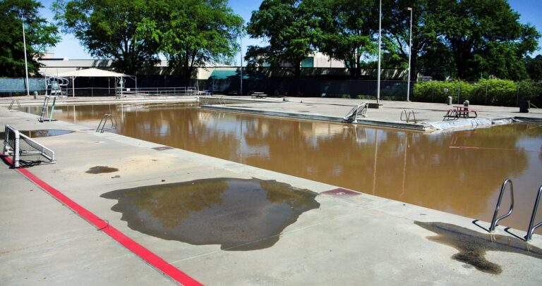 Piscine de villa vidée bordée de dalles claires et de transats sous un ciel dégagé