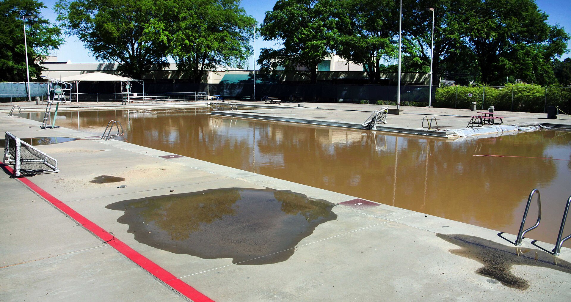 Piscine de villa vidée bordée de dalles claires et de transats sous un ciel dégagé