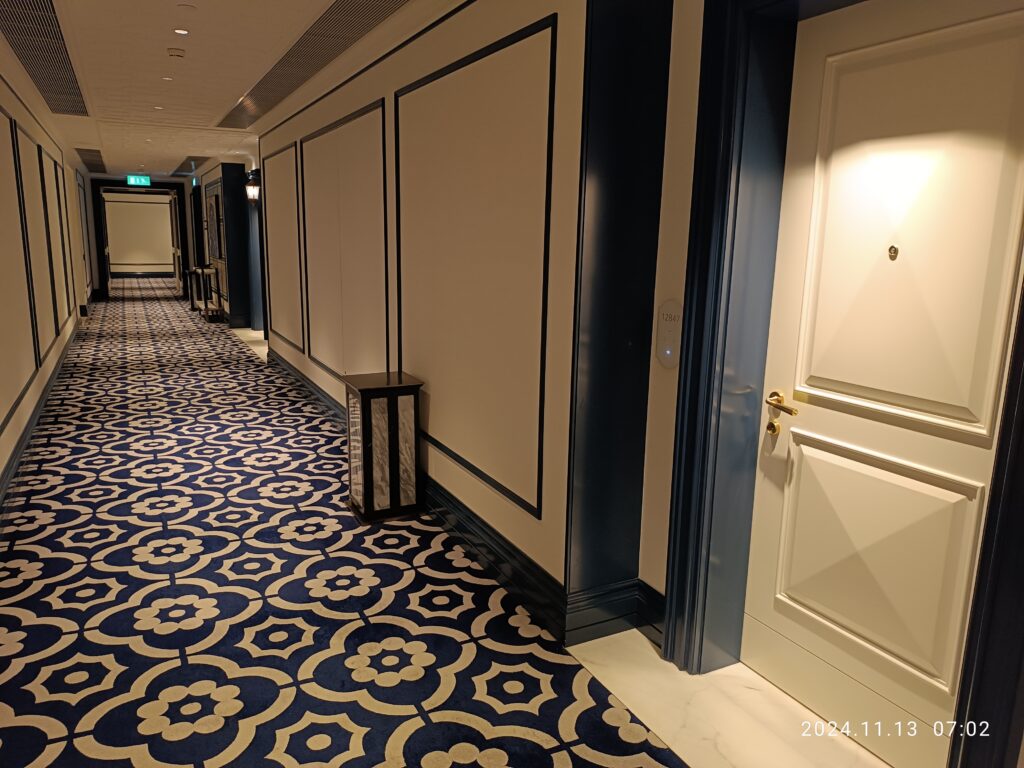 Couloir d'hôtel moquetté bordé de portes numérotées et éclairé par des appliques murales