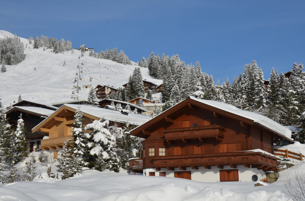 Façade de chalet en bois sombre aux balcons sculptés, toit chargé de neige et volets clairs