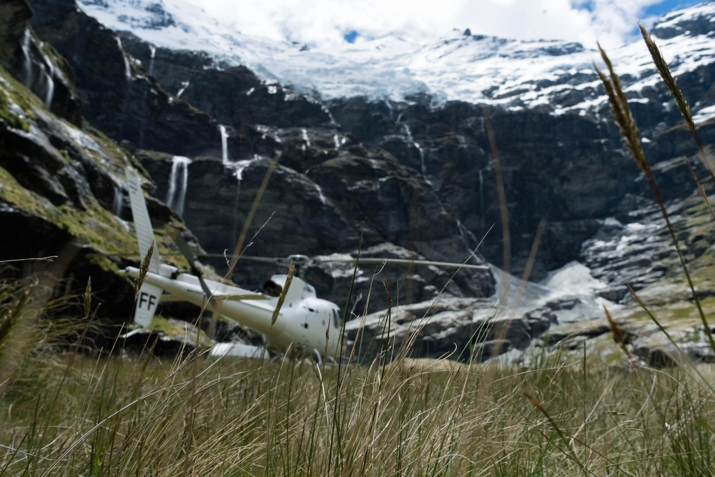 Hélicoptère posé sur une aire damée en altitude, rotor à l'arrêt et sommets en arrière-plan