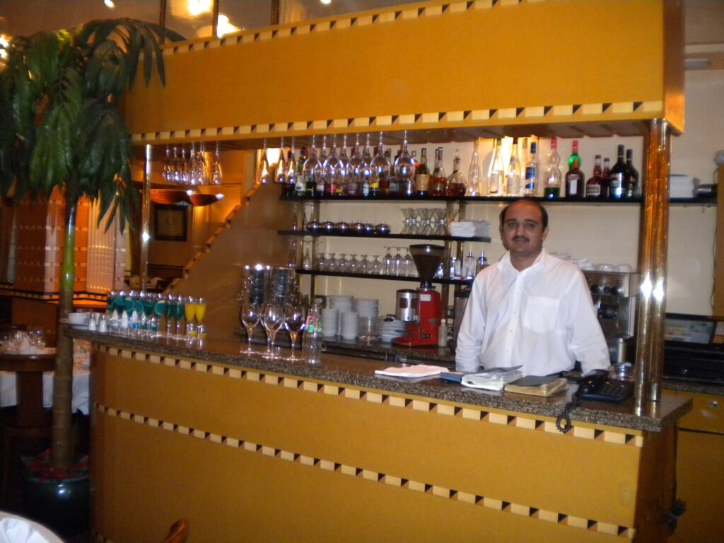 Employé d'hôtel en uniforme traversant un couloir moquetté avec un plateau de service