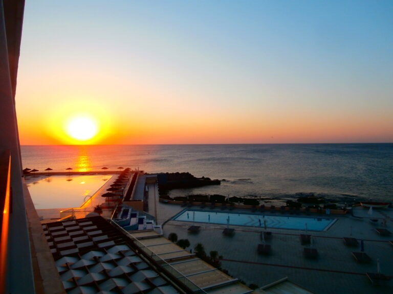 Terrasse de resort méditerranéen avec piscine à débordement face à la mer en fin de journée