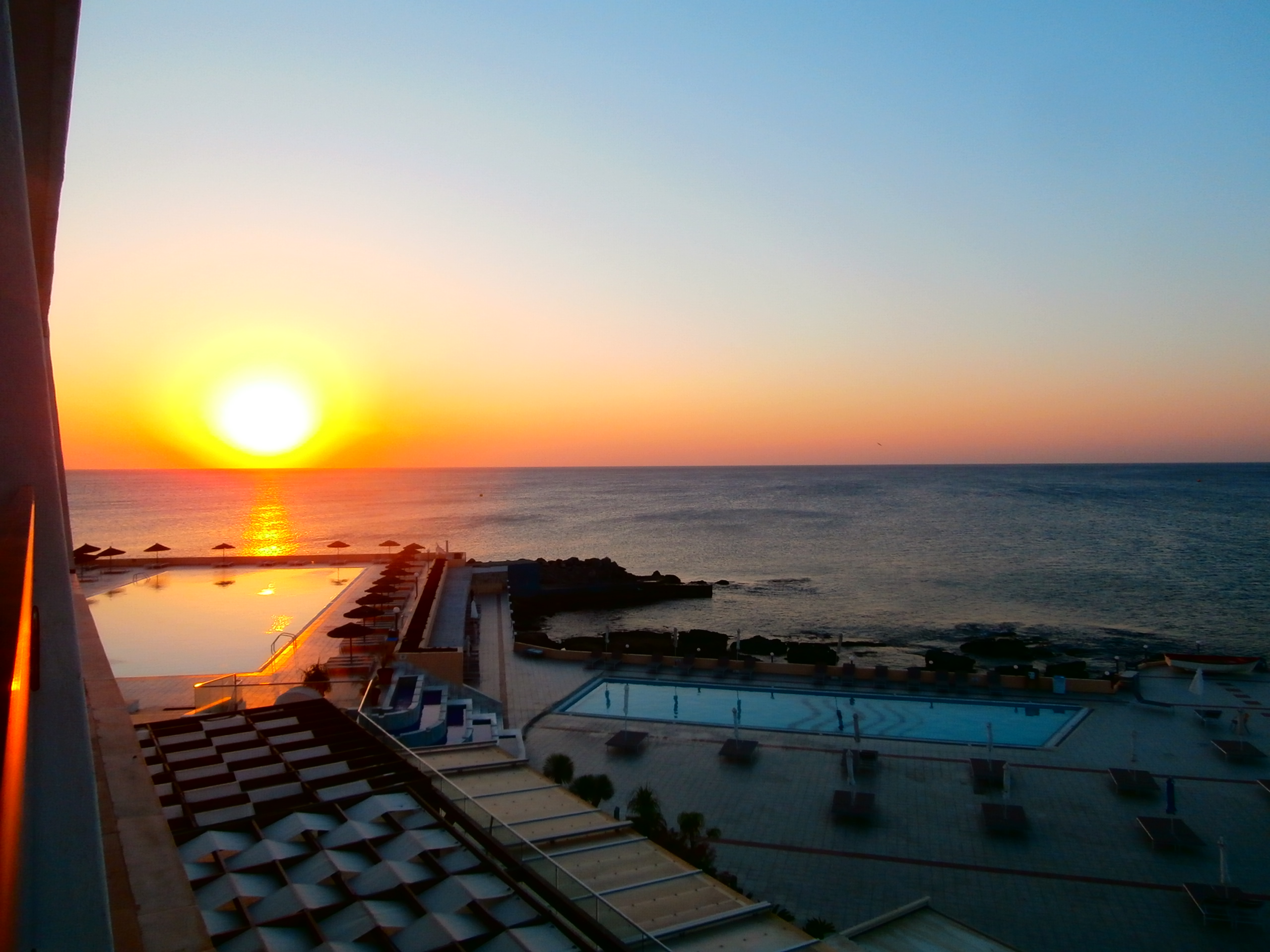 Terrasse de resort méditerranéen avec piscine à débordement face à la mer en fin de journée