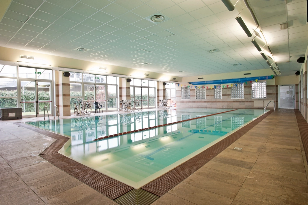 Bassin int&eacute;rieur d'h&ocirc;tel vide et &eacute;clair&eacute;, entour&eacute; de transats vides et de baies vitr&eacute;es